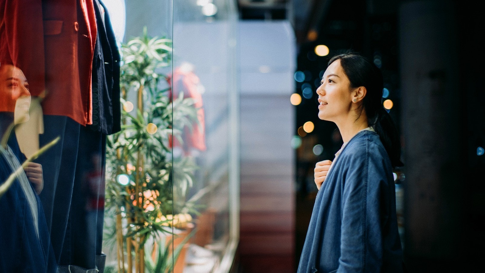 Young Asian woman looking at shop window while walking in the city at night
