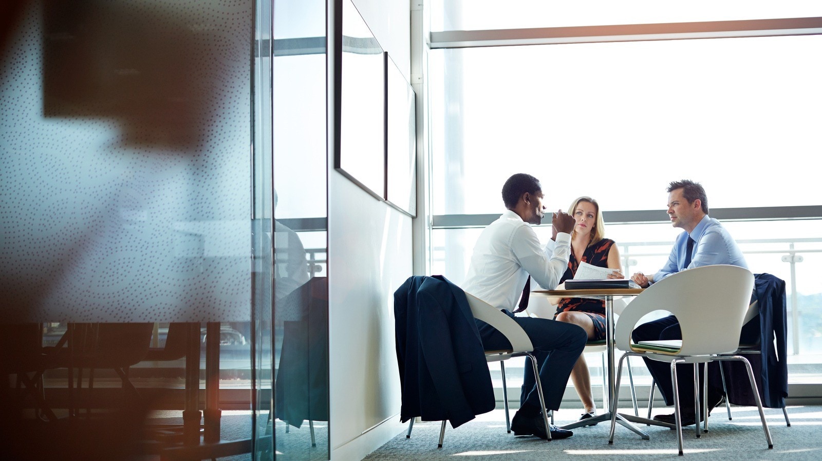 Two people discussing work at small table in modern office meeting area.