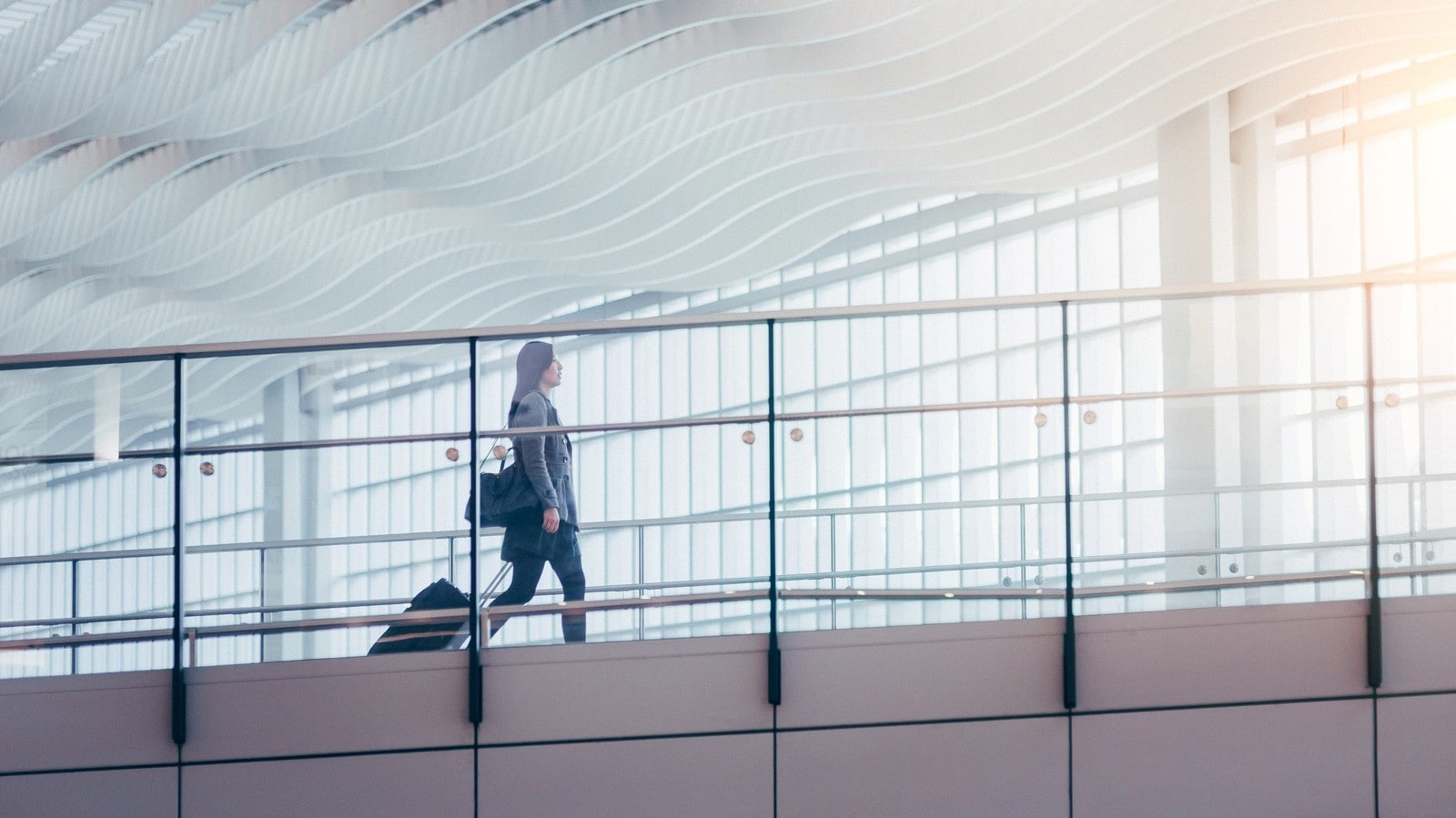 Person pulling wheeled luggage across a modern airport walkway.