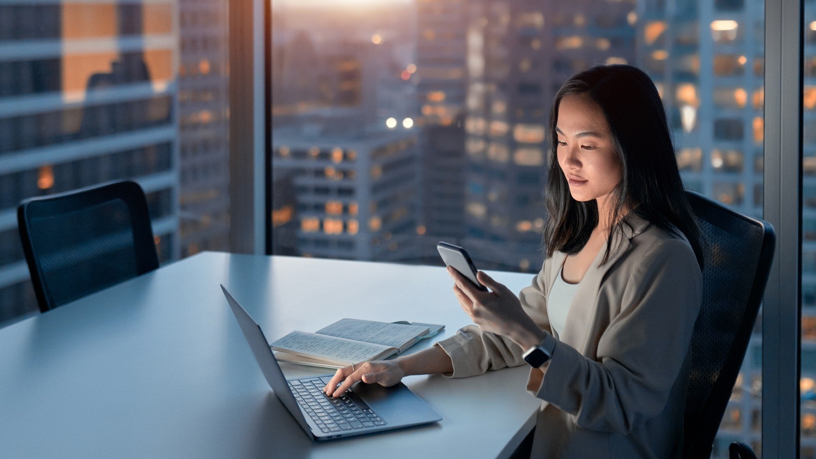 A female office worker looking at her mobile phone while sitting on an office desk