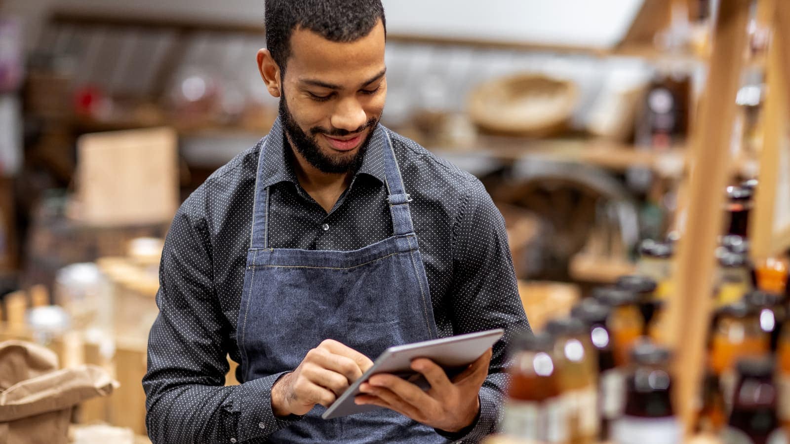 Hospitality worker looking down at tablet, wearing an apron