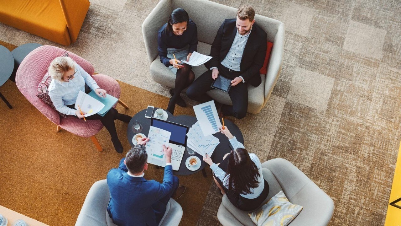 Business team meeting in a modern lounge area, discussing documents and charts around a coffee table.