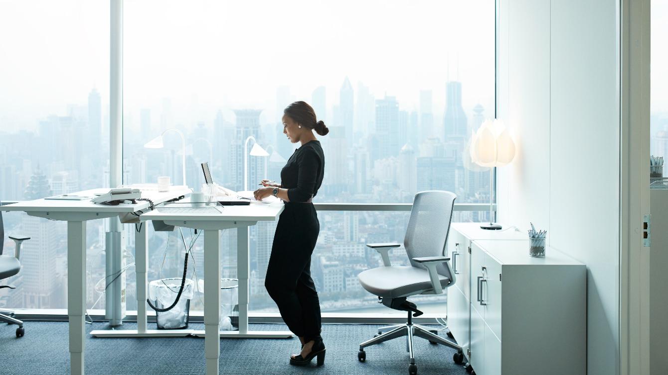 Woman working at a standing desk in front of a large window with skyline views